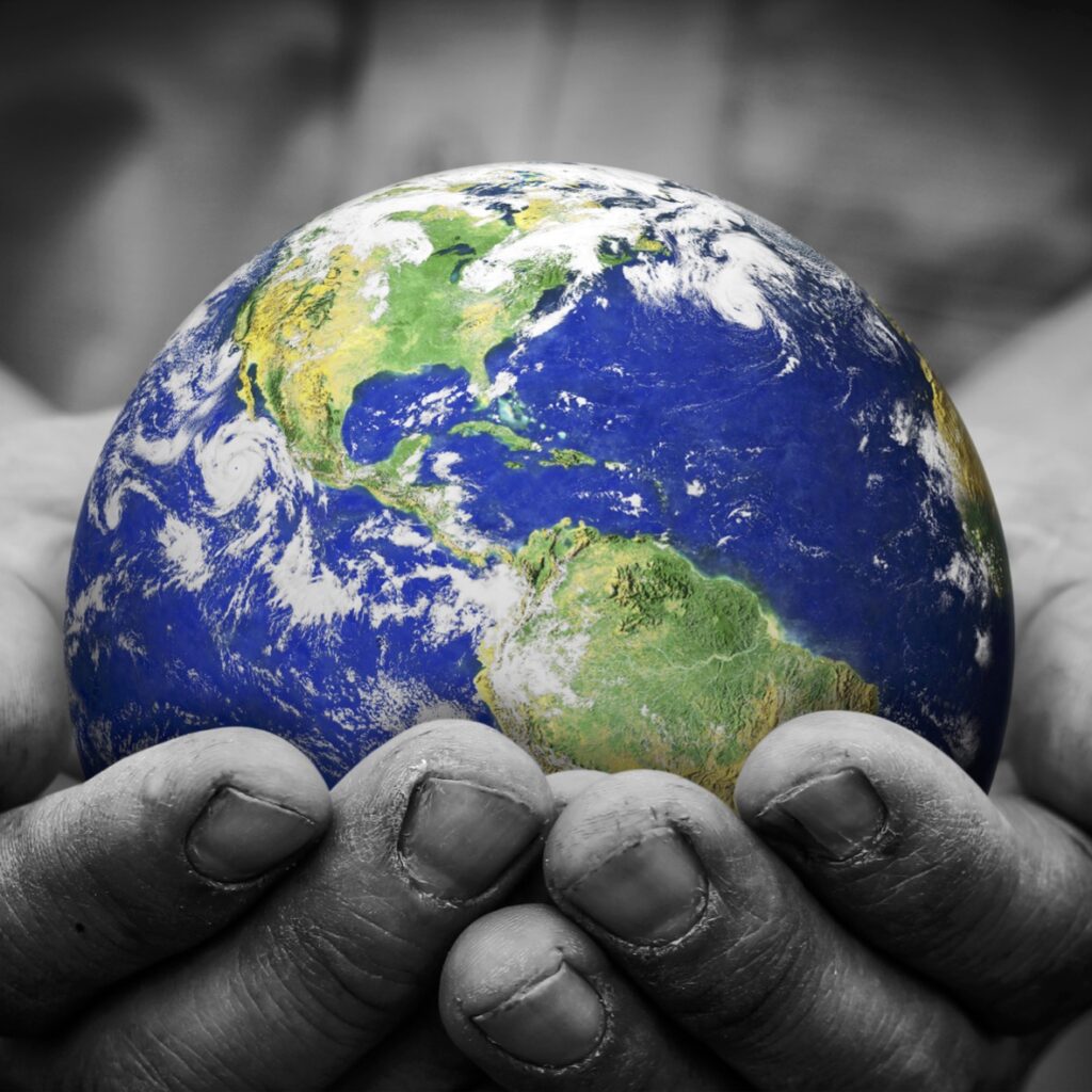 Two hands cradle an earth globe. The hands are photographed in black and white, but the earth is vibrant with greens, blues and swirling white clouds.