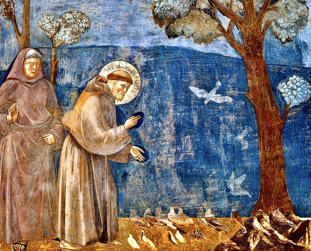 St Francis wears a brown habit and is preaching to a flock of birds with outstretched hands. Another friar stands behind him. There are trees on blue background.