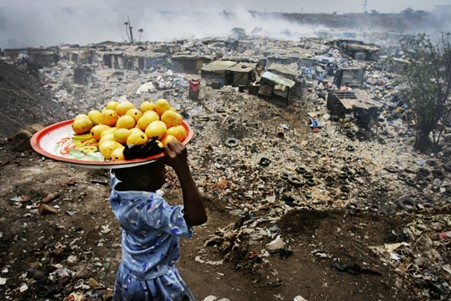 Hundreds of thousands of tonnes of plastic waste are exported overseas every year.  A girl carrying fruit on her head descends on a village at the Olusosun landfill site, Nigeria's largest trash heap comprising over 100 acres of garbage. Credit: Jacob Silberberg / Panos
